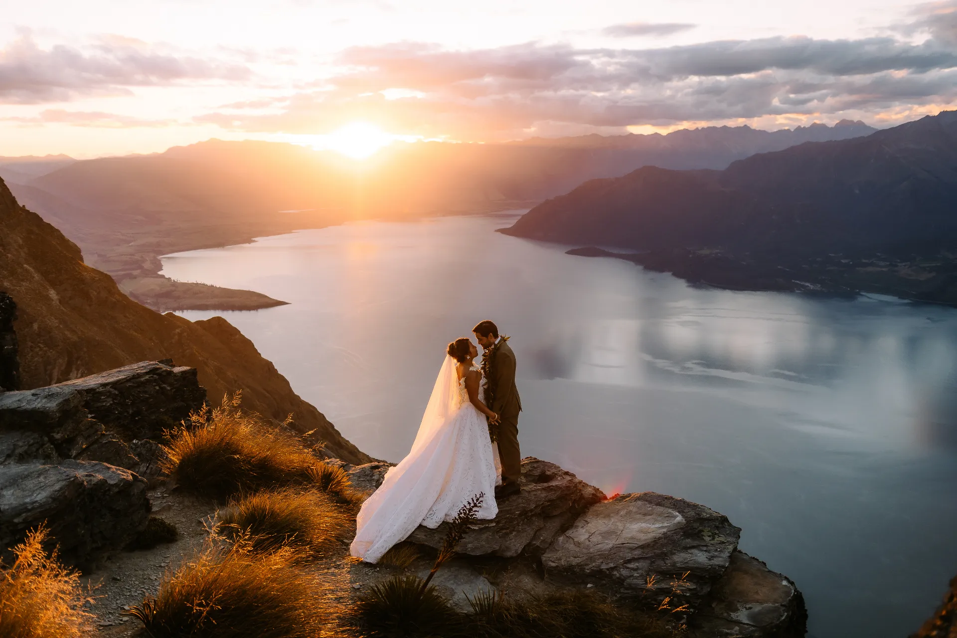 Couple standing on a mountain peak above Lake Wakatipu at sunset during a Queenstown elopement