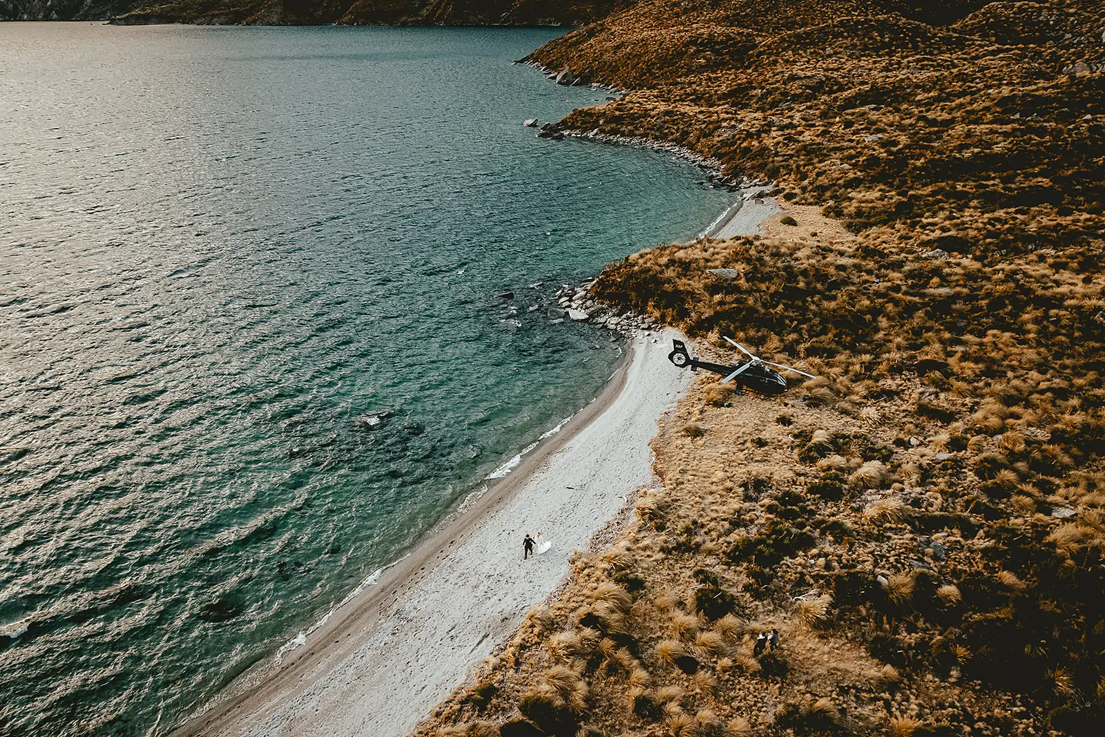 Aerial view of a helicopter on an alpine beach at Lochnagar with a couple beside it